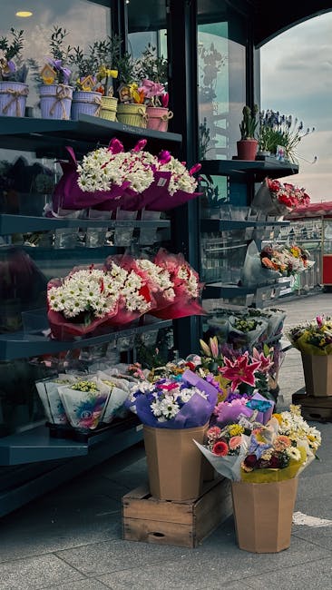 A display of fresh floral arrangements and bouquets at a flower shop near Twickenham Stadium. The flowers include white chrysanthemums, pink lilies, purple irises, and mixed pastel-colored blooms, arr